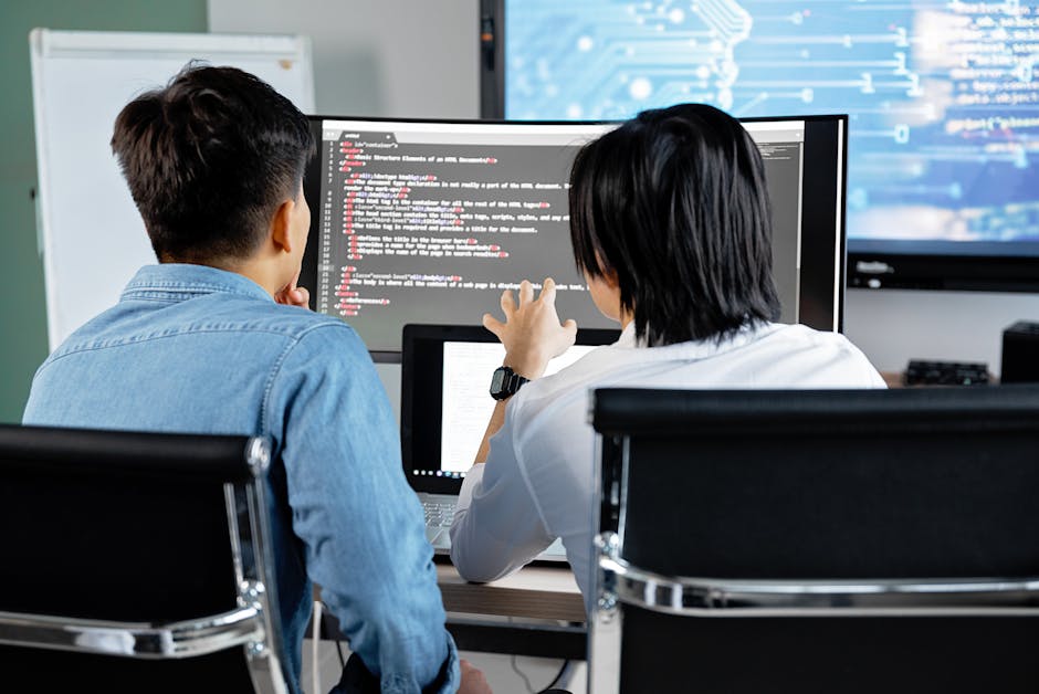 Two developers working together in an office, discussing code on a screen