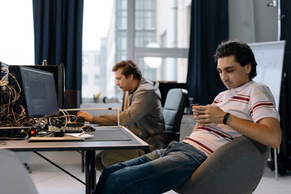 Two men working in a modern office, one on a computer and the other on a smartphone