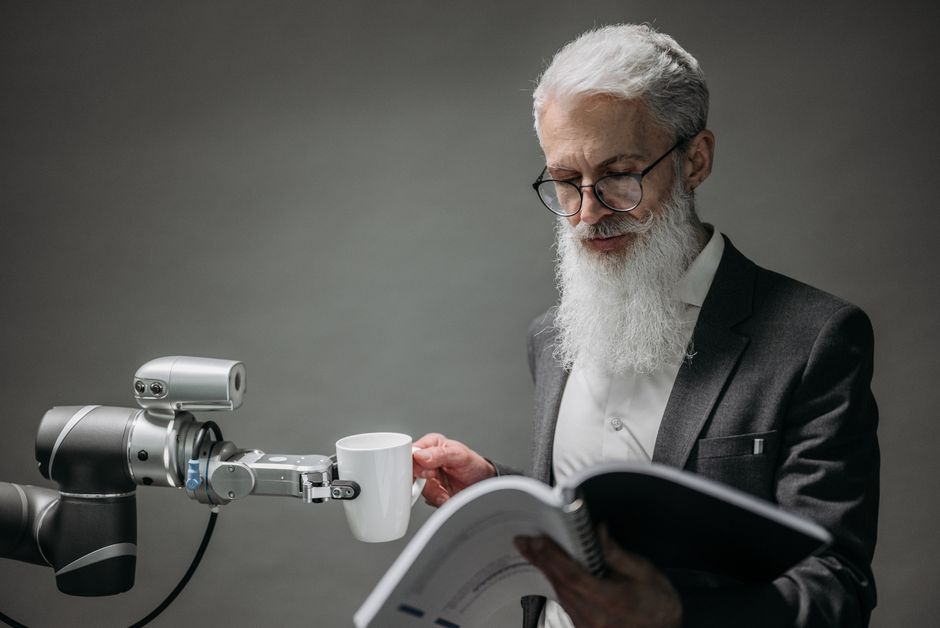 Senior man interacts with robotic arm and cup in a modern studio environment.